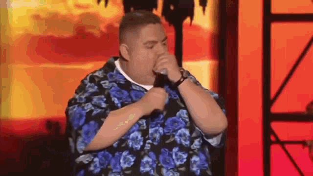 a man in a blue and black floral shirt is singing into a microphone on a stage .