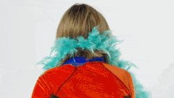 a woman wearing a red and blue feather boa is standing in front of a white wall .