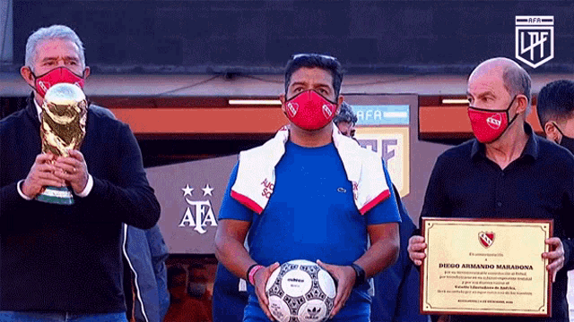 a man wearing a mask holds a soccer ball and a certificate