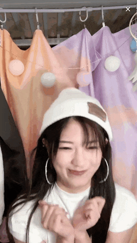 a girl wearing a white hat and hoop earrings is making a heart shape with her hands