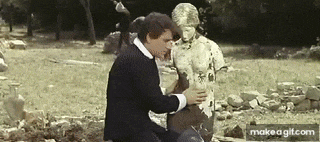 a man in a suit is kneeling down next to a statue of a woman .
