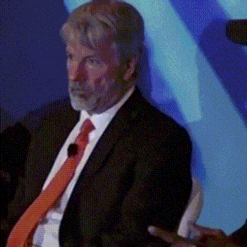 a man in a suit and tie is sitting in front of a blue wall .