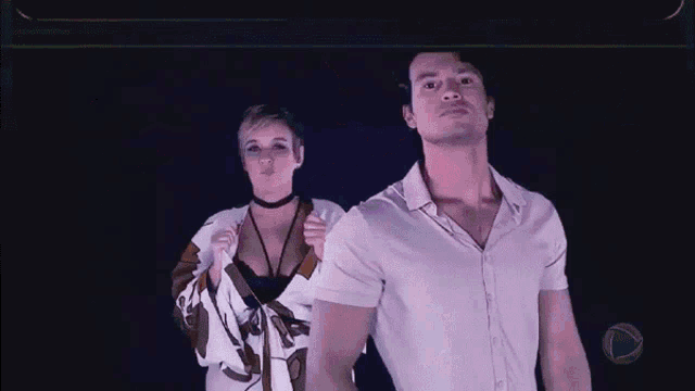a man and a woman are standing next to each other in a dark room . the woman is wearing a choker .