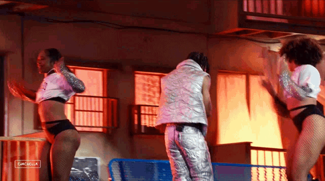a man and two women are dancing in front of a sign that says coachella on it