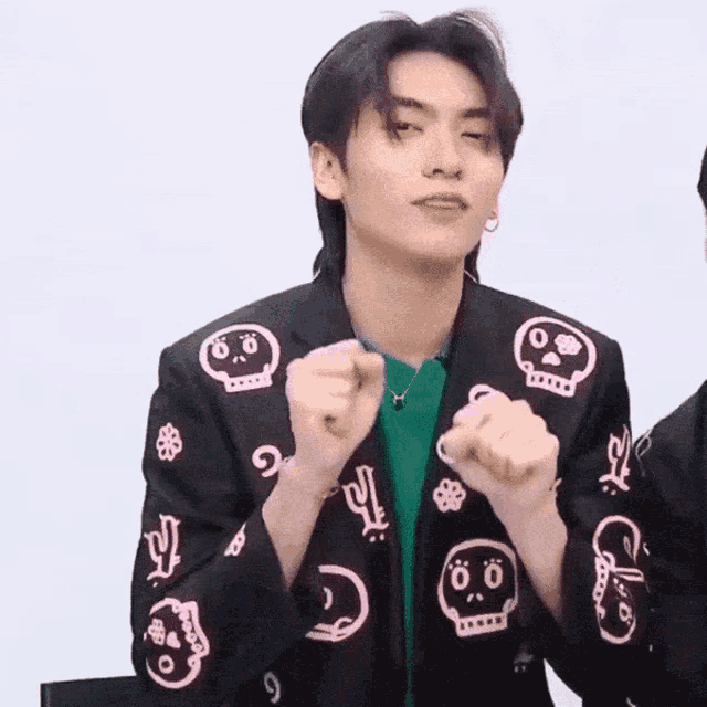 a young man wearing a jacket with skulls on it is making a fist .
