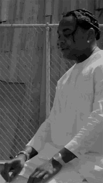 a black and white photo of a man sitting in front of a fence