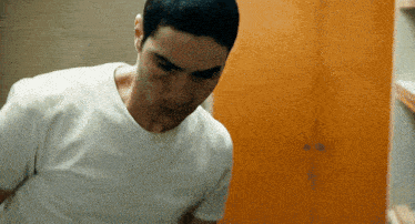 a man in a white shirt is standing in front of a orange wall