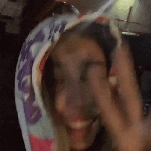 a woman wearing a colorful hoodie is smiling and covering her face