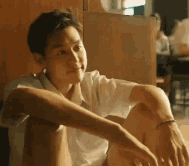 a young man is sitting on the floor with his legs crossed and his arm resting on his lap .