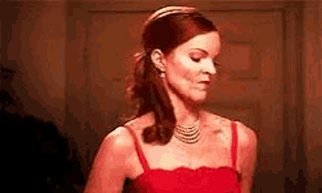 a woman in a red dress and necklace is standing in a room .