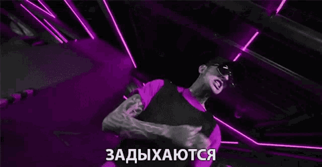a man wearing sunglasses and a purple shirt is standing in a dark room with neon lights .