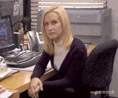 a woman is sitting at a desk with her hands folded in front of her .