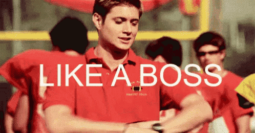 a man in a red shirt is looking at his watch with the words like a boss behind him .