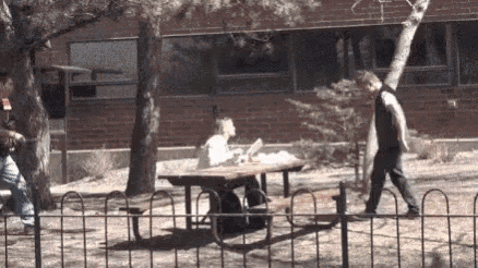a man walking past a woman sitting at a picnic table in a park