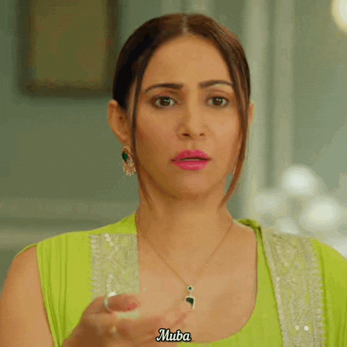 a woman in a green top is holding a glass with the name muba written on her face