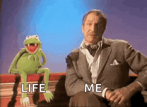 kermit the frog is sitting on a couch next to a man in a suit and tie .
