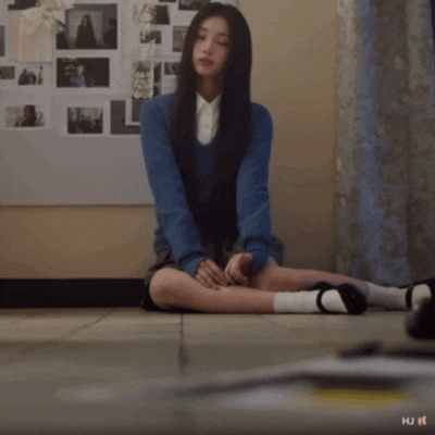 a girl in a blue sweater and white shirt sits on the floor