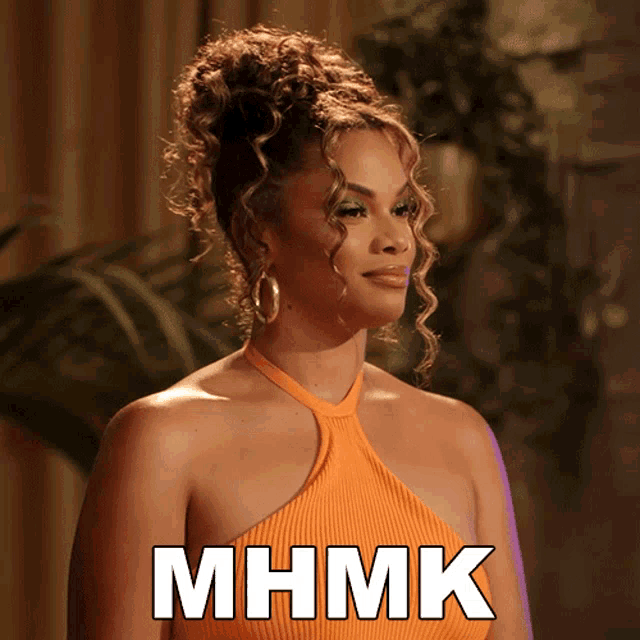 a woman with curly hair is wearing an orange top and the caption mhmk is above her