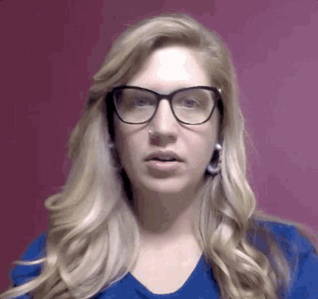 a woman wearing glasses and earrings is making a funny face in front of a pink wall .