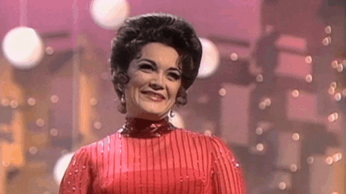 a woman in a red dress is smiling on a stage in front of christmas lights .