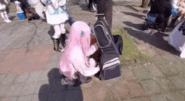 a girl in a pink wig is kneeling down next to a black bag