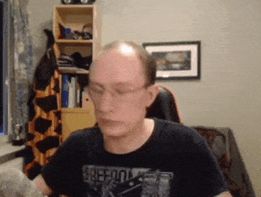 a bald man wearing glasses and a black shirt that says ' freedom ' on it