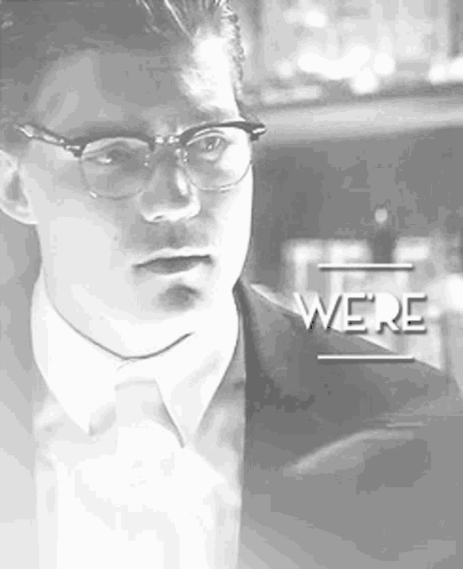 a man wearing glasses and a suit and tie is standing in a black and white photo .