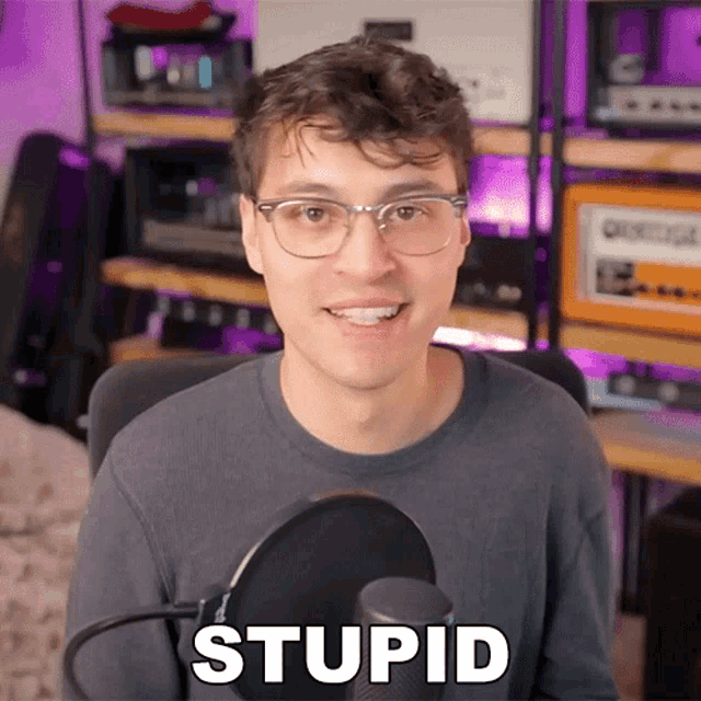 a man wearing glasses stands in front of a microphone and says stupid in white letters