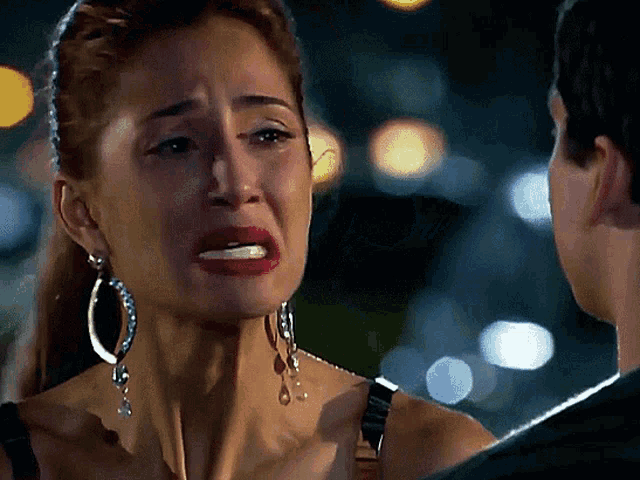 a woman wearing hoop earrings is crying with a man in the background
