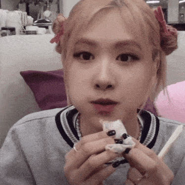 a woman with black nails is eating a piece of food with chopsticks