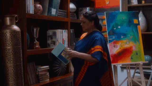 a woman is reading a book in front of a painting on an easel