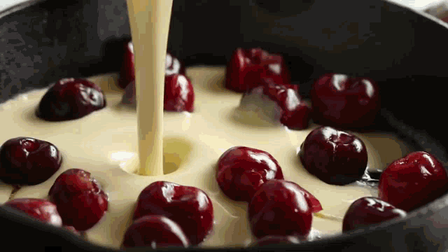 a skillet filled with cherries and batter being poured into it