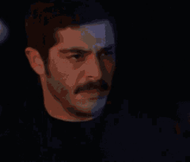 a close up of a man 's face with a mustache in a dark room .