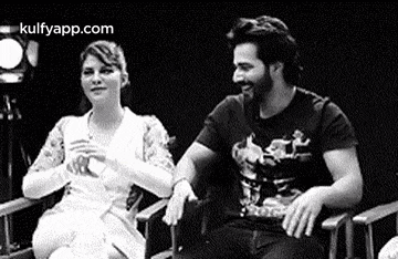 a black and white photo of a man and a woman sitting next to each other .