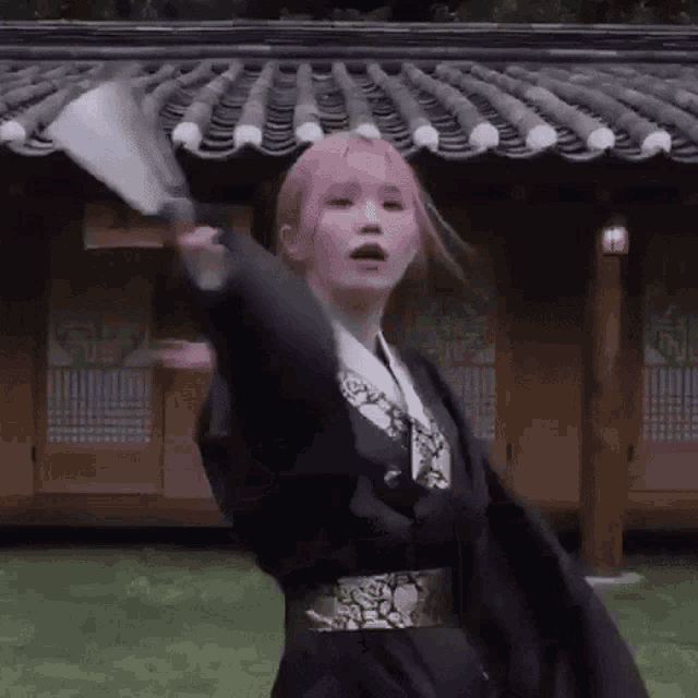 a girl with pink hair is holding a fan in front of a roof .