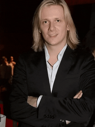 a man with long blonde hair is wearing a white shirt and grey jacket