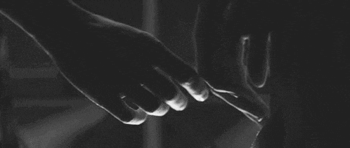 a black and white photo of two people holding hands in the dark .