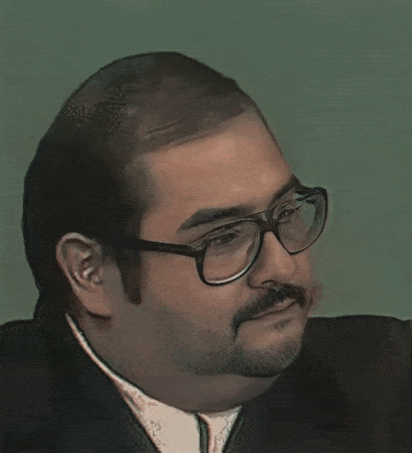 a man with glasses and a beard is wearing a black suit and white shirt