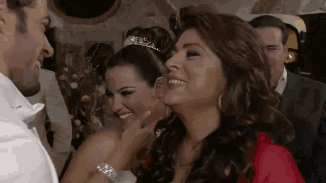 a woman wearing a tiara is smiling while a man touches her face