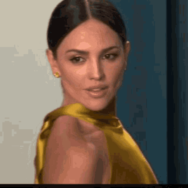 a woman in a yellow dress is looking at the camera and smiling .