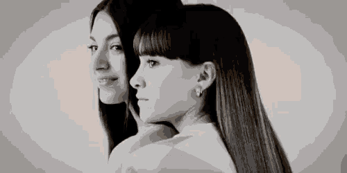 a black and white photo of two women standing next to each other with their backs to the camera .