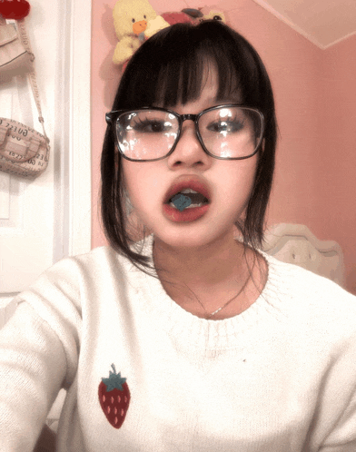 a girl wearing glasses and a sweater with a strawberry embroidered on it