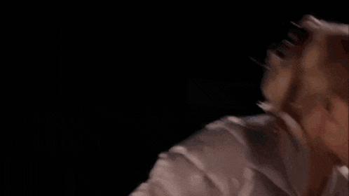 a woman in a white shirt is screaming with her mouth open in a dark room .