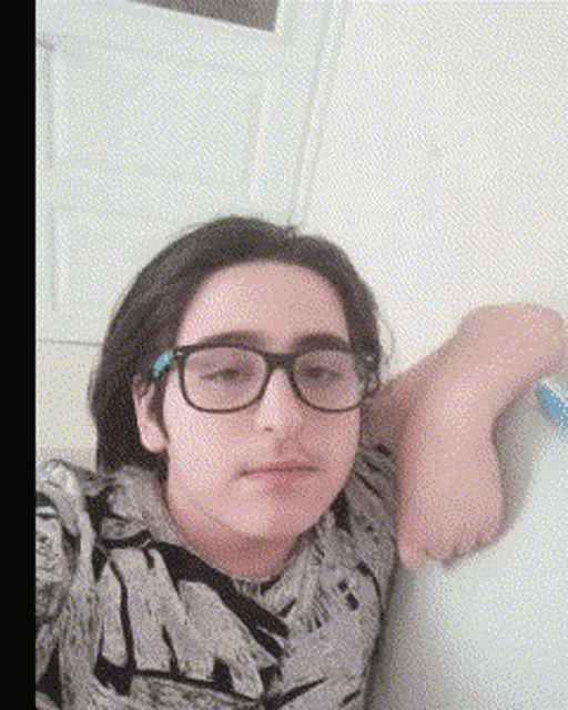 a young girl wearing glasses and a floral shirt is leaning on a wall