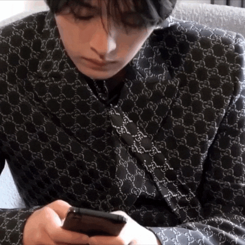 a man wearing a gucci shirt is looking at his cell phone