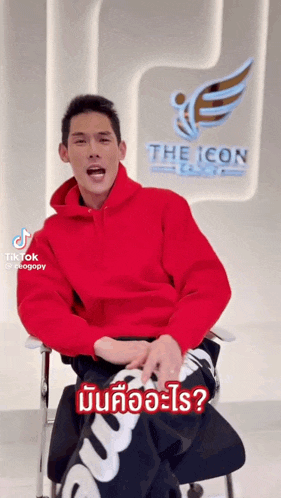 a man in a red hoodie is sitting in a chair in front of a sign that says the icon