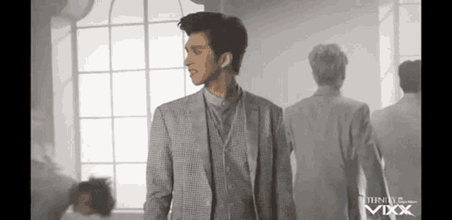 a man in a suit is standing in front of a window in a room with other men .