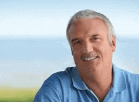 a man in a blue shirt is smiling for the camera while sitting outside .