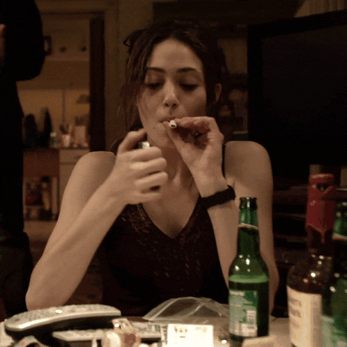 a woman is smoking a cigarette next to a bottle of beer and a remote control
