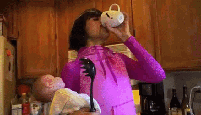 a woman in a pink shirt is drinking from a cup while holding a baby